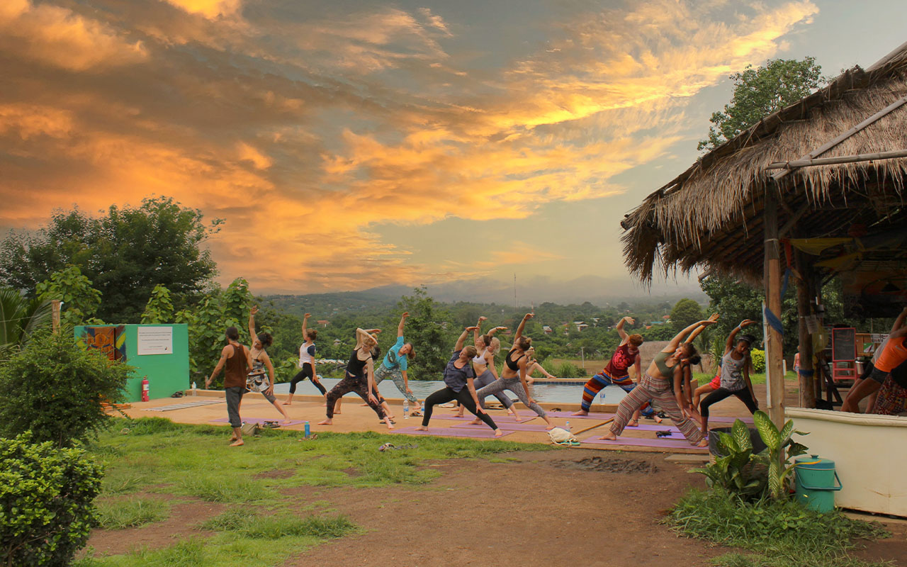 Group practicing yoga outdoors at sunset in Pai, Thailand
