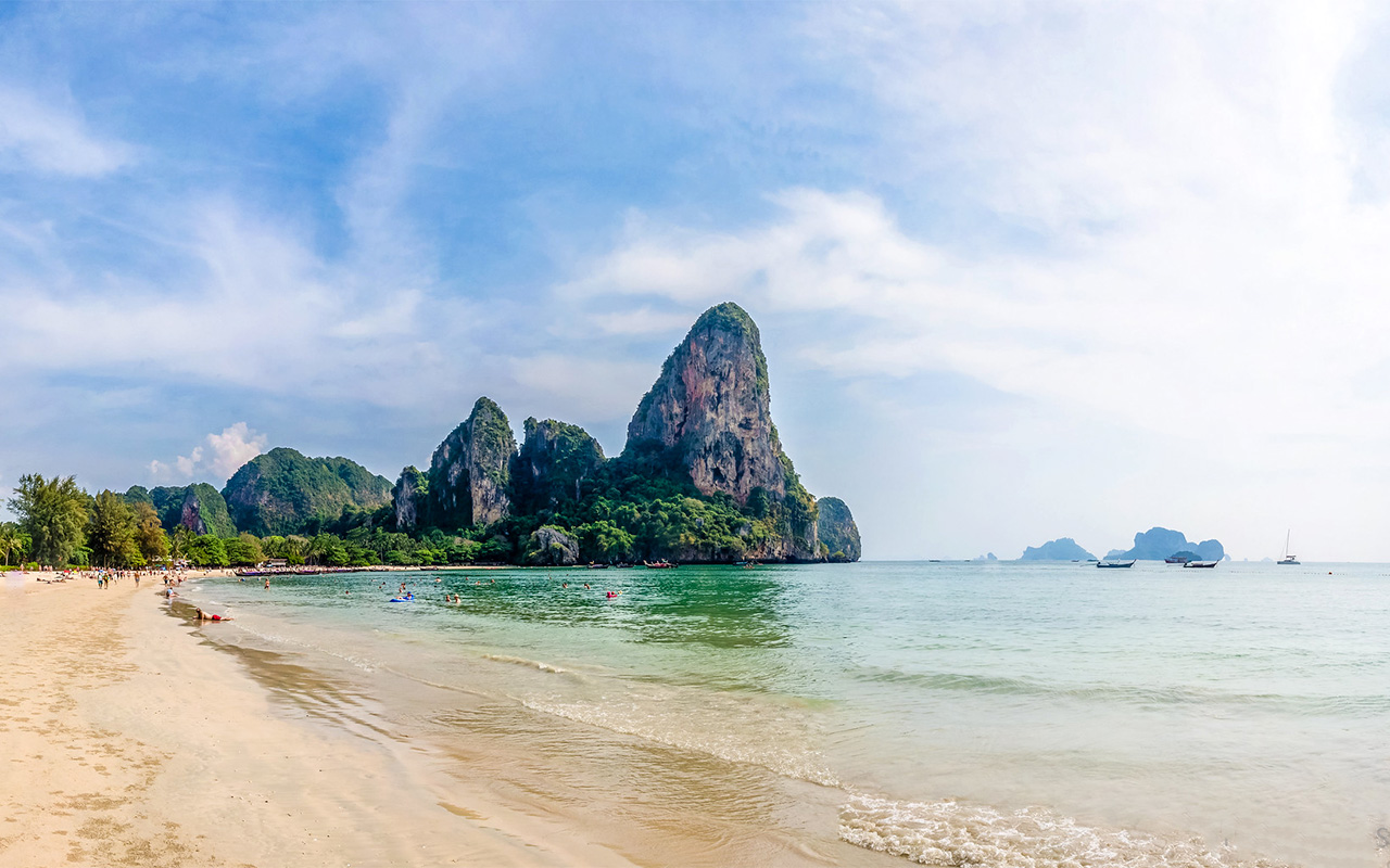 Scenic view of Railay Beach in Krabi, Thailand, with limestone cliffs, clear turquoise water, and traditional longtail boats on the shore