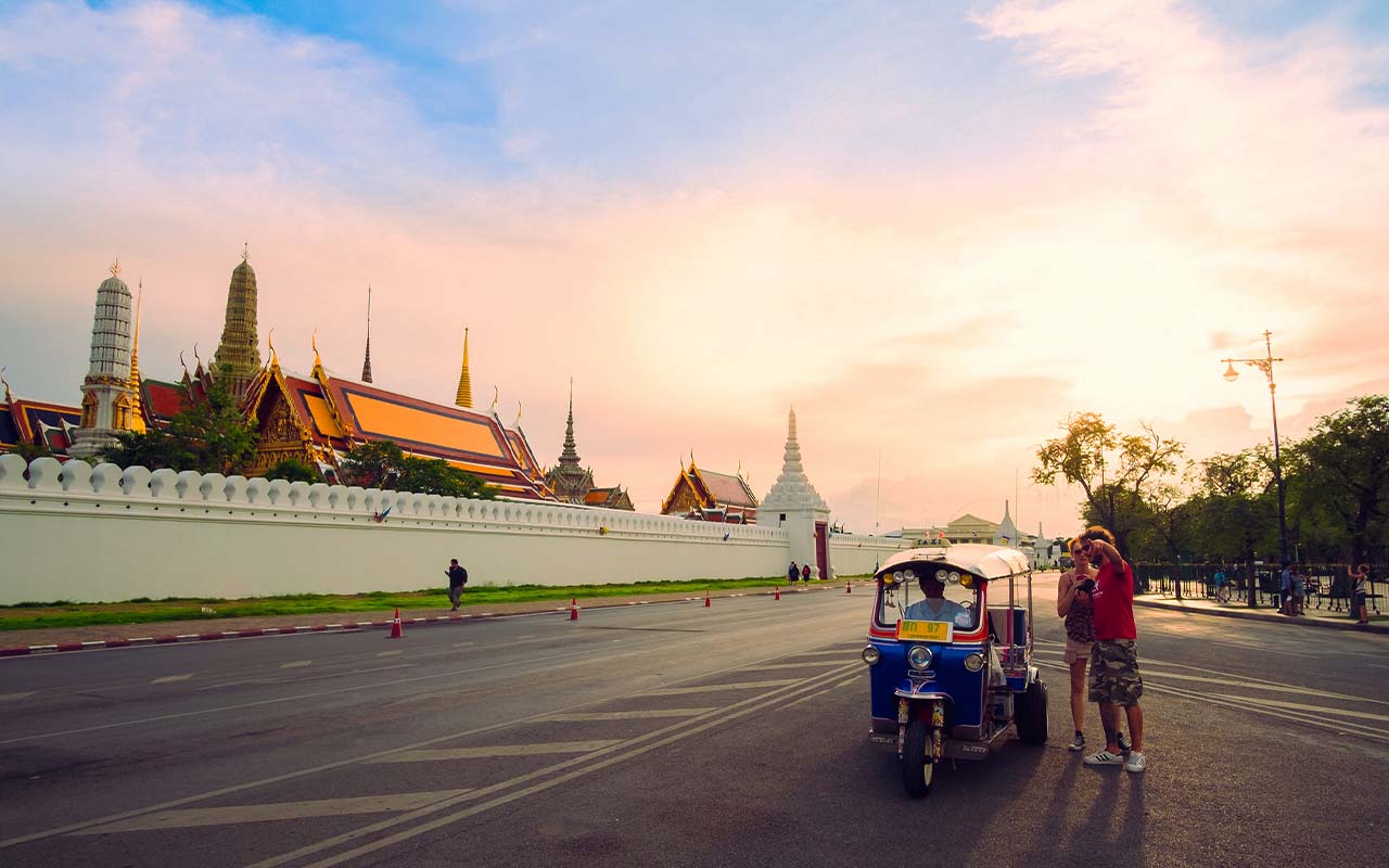 Tourists posing beside a blue tuk‑tuk outside Bangkok’s Grand Palace at sunset